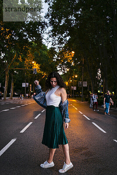 Junge Frau in Jeansjacke posiert auf der Straße in einem Park in der Abenddämmerung