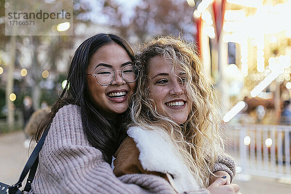 Cheerful female friends embracing at amusement park