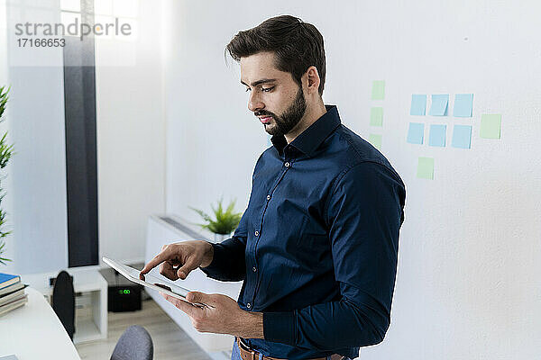 Male entrepreneur using digital tablet against wall in office