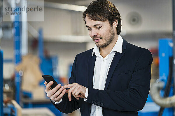 Young businessman using mobile phone while standing at industry
