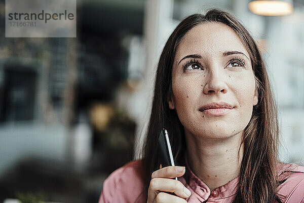 Nachdenkliche Frau mit Mobiltelefon  die in einem Café nach oben schaut