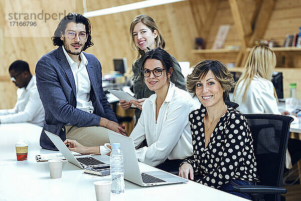 Lächelndes Business-Team mit Laptop  das am Schreibtisch in einem Coworking Space kreative Ideen entwickelt