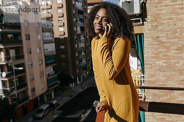 Frau mit lockigem Haar  die auf dem Balkon stehend mit ihrem Handy telefoniert