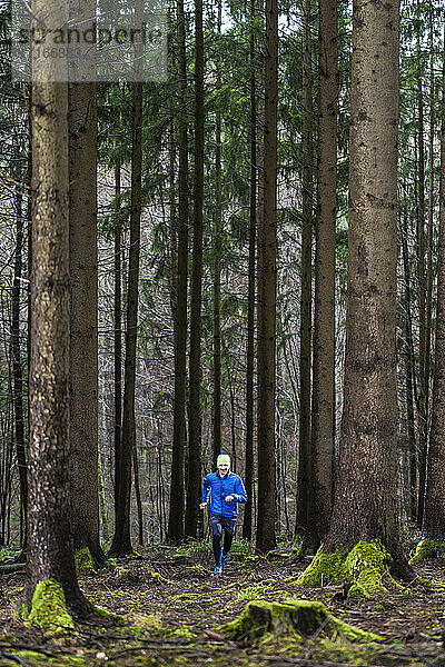 Männlicher Jogger in blauer Jacke läuft im Wald