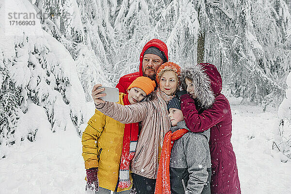 Reife Frau  die selfie mit Familie beim Stehen im Wald während snowing