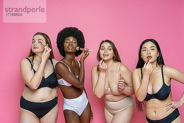 Multi-ethnische Gruppe von weiblichen Modellen in Dessous  die sich vor einem rosa Hintergrund schminken