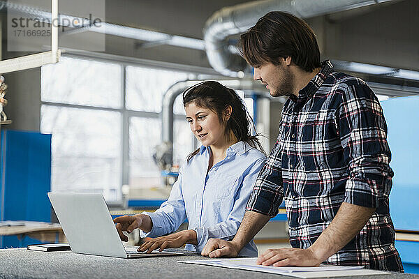Expertise having discussion over laptop while standing by colleague at industry