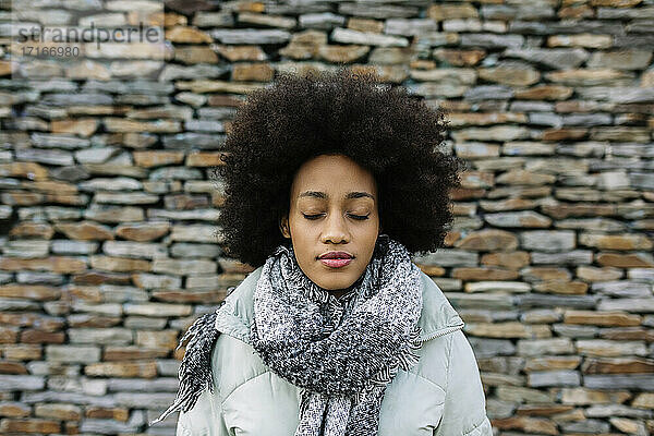 Afro junge Frau mit geschlossenen Augen gegen Steinwand im Winter