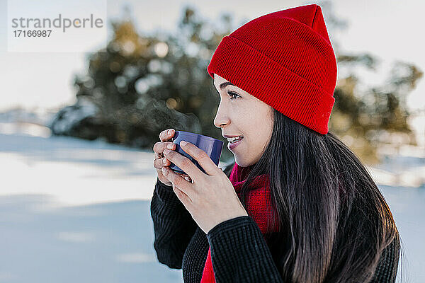 Lächelnde Frau trinkt Kaffee und genießt den Winter auf dem Lande