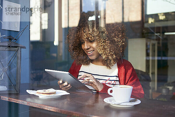 Smiling Afro woman using digital tablet while sitting at cafe