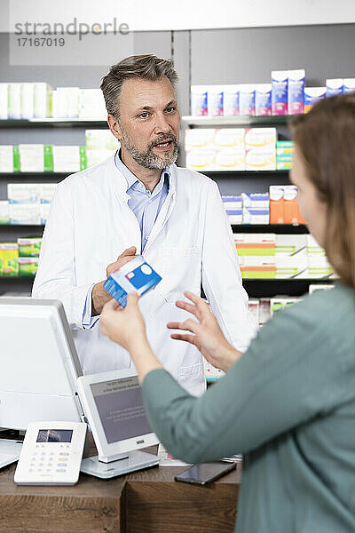 Mature pharmacist advising customer about medicine at checkout in store