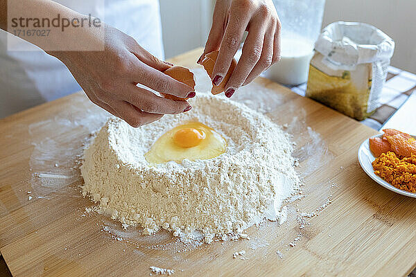 Woman breaking egg in flour on cutting board in kitchen