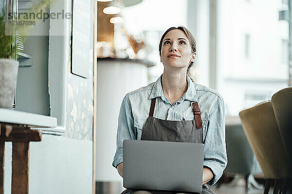 Unternehmerin mit Laptop  die in einem Café nach oben schaut