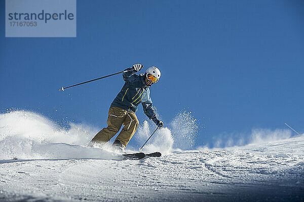 Young man skiing on snow against blue clear sky