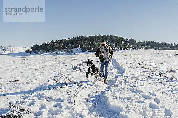 Verspielter Mann mit Hund läuft im Schnee an einem sonnigen Tag