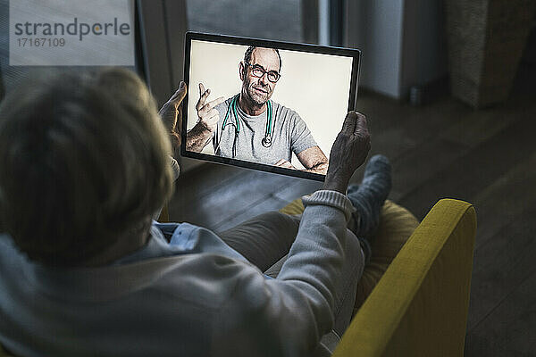 Älterer Patient lässt sich von einem männlichen Arzt per Videoanruf beraten  während er in einem dunklen Raum sitzt