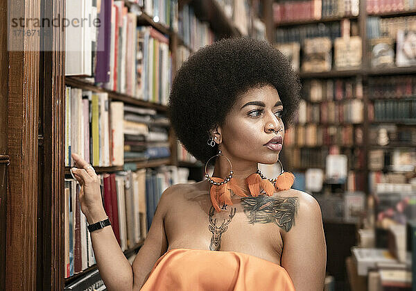 Thoughtful young woman looking away by bookshelf at library