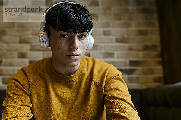 Junger Mann mit Kopfhörern  der im Café sitzt und starrt