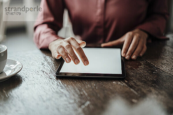 Die Hand einer Geschäftsfrau benutzt ein digitales Tablet am Tisch in einem Café