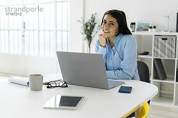 Geschäftsfrau mit Headset  die lächelnd mit einem Laptop im Büro sitzt