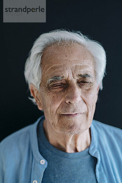 Älterer Mann stehend mit geschlossenen Augen vor schwarzem Hintergrund