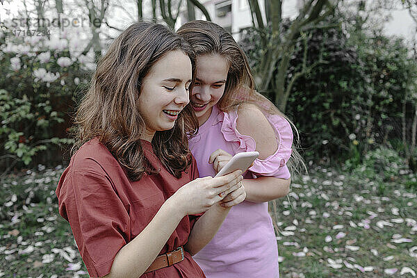 Smiling teenage female friends looking at mobile phone in public park