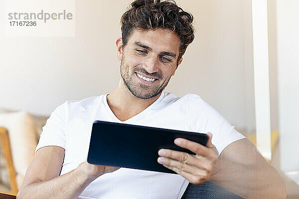 Mittelgroßer erwachsener Mann  der zu Hause sitzend ein digitales Tablet benutzt