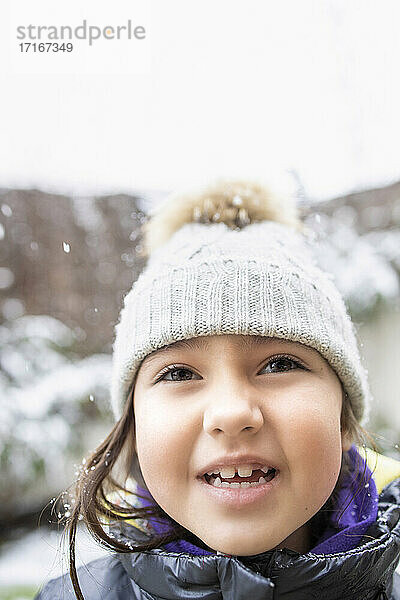 Cute smiling girl in knit hat during snowfall