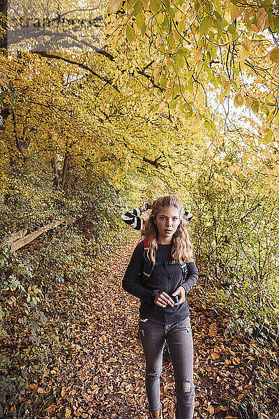 Girl hiking while walking with friend in background at forest during autumn