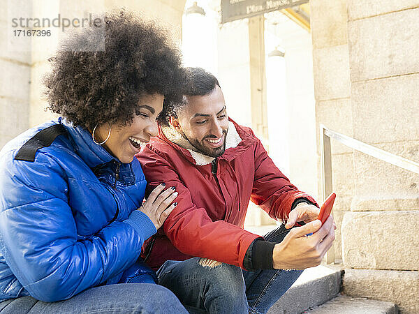 Happy friends using smart phone while sitting on steps