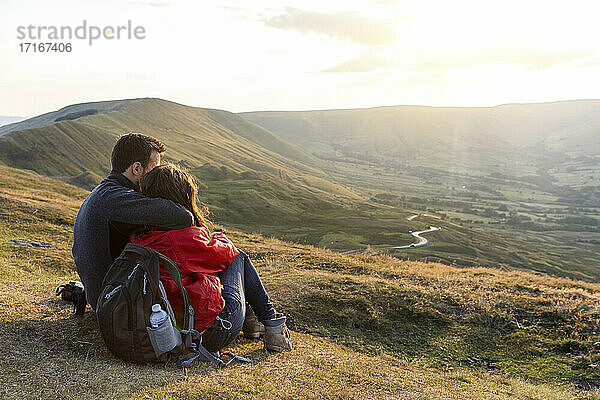 Junges Paar  das sich umarmt  während es den Sonnenuntergang im Urlaub betrachtet