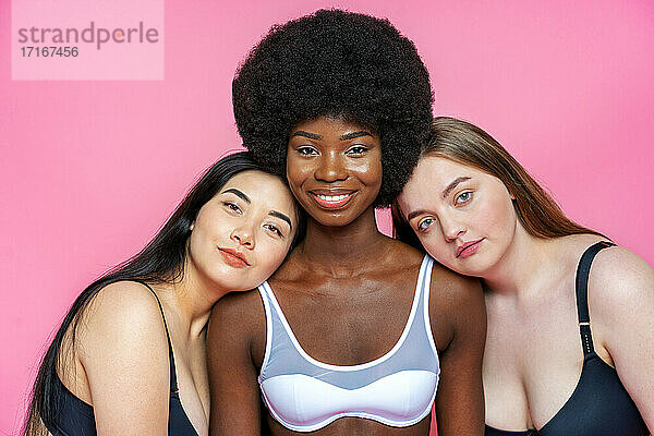 Multi-ethnische weibliche Modelle in Dessous lehnen sich an die Schulter einer Afro-Frau vor einem rosa Hintergrund