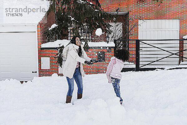 Mutter und Tochter spielen mit Schnee vor dem Haus im Winter