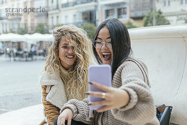 Cheerful female friends taking selfie through smart phone