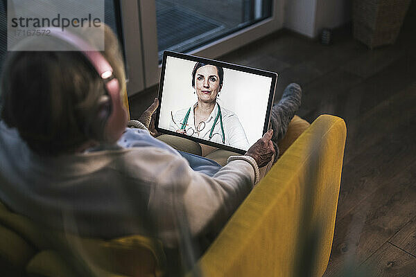 Ältere Frau bei einem Videogespräch mit einer Ärztin über ein digitales Tablet in einem dunklen Raum