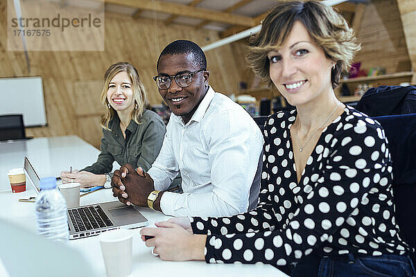 Lächelnder Geschäftsmann und Geschäftsfrau sitzen am Schreibtisch in einem Coworking-Büro