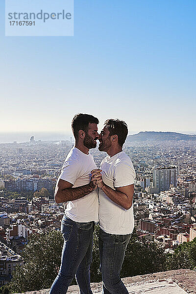 Schwule Männer  die sich umarmen  während sie an einem sonnigen Tag vor einer Stadtlandschaft stehen  Bunkers del Carmel  Barcelona  Spanien