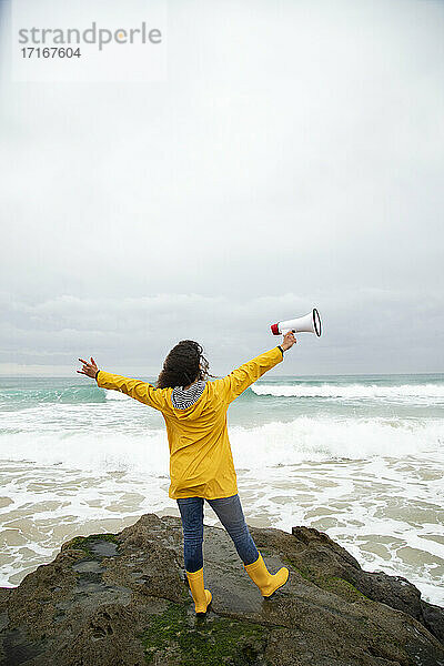 Unbekümmerte junge Frau  die ein Megaphon hält  während sie am Meer steht