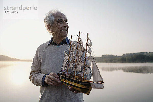 Lächelnder älterer Mann  der ein Spielzeugboot hält  während er am See steht