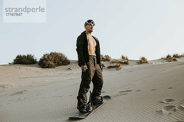 Junger Mann trägt ein Sandboard und steht auf Sand in Almeria  Tabernas-Wüste  Spanien