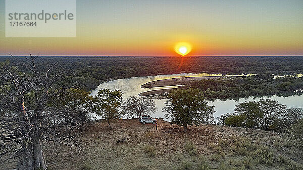 Luftaufnahme eines Jeeps mit einem Dachzelt in der Nähe des Flusses und eines großen Affenbrotbaums bei Sonnenuntergang  Cunene-Flussgebiet  Angola