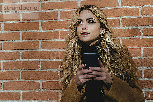 Blond woman with smart phone listening music while looking away