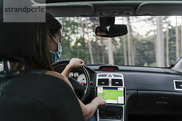 Frau mit Gesichtsmaske benutzt GPS beim Autofahren