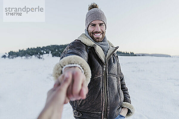 Lächelnder Mann  der die Hand einer Frau hält  während er im Schnee vor einem klaren Himmel steht