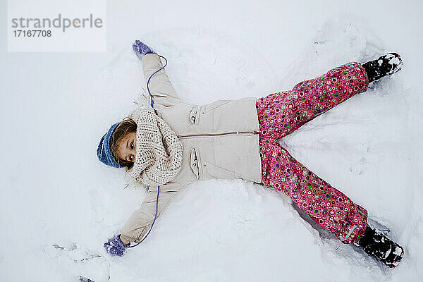Verspieltes Mädchen macht Schneeengel im Winter