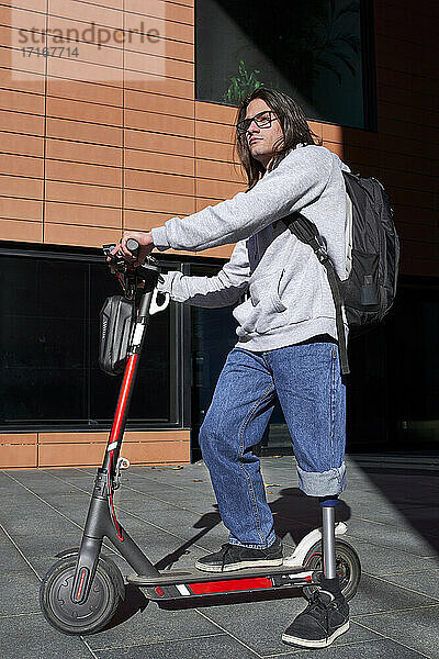 Disabled man with artificial limb standing on electric push scooter against building