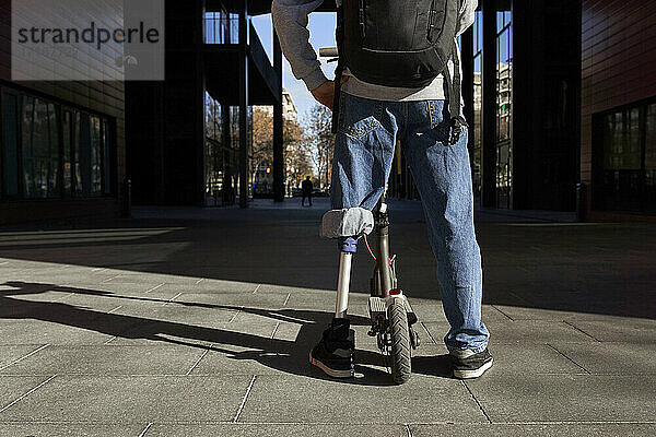 Young disabled man standing on footpath with electric push scooter in city