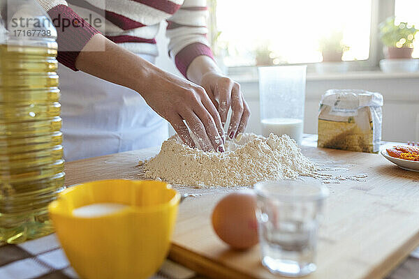 Woman making heap of flour in kitchen at home