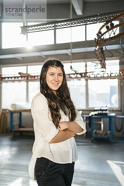 Confident businesswoman smiling while standing with arms crossed at industry