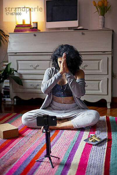 Spiritual woman with hands clasped sitting at home during video call